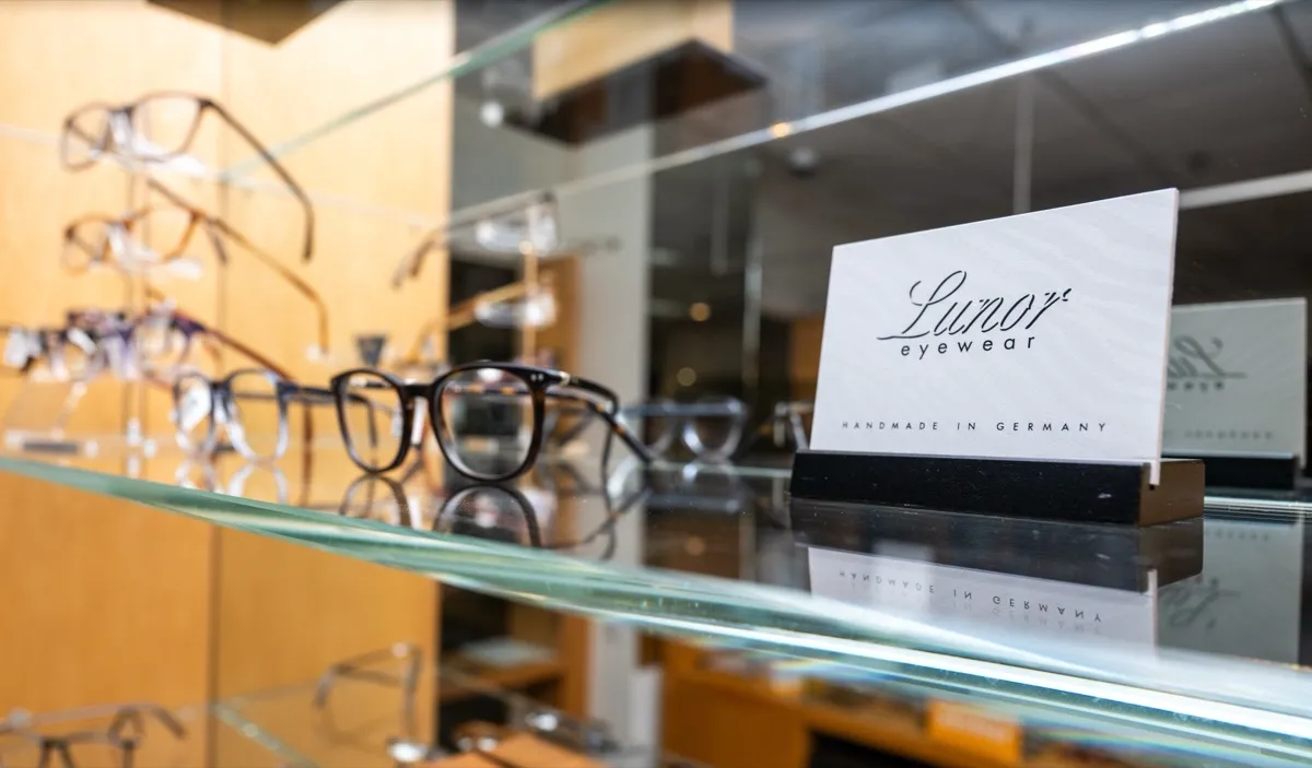 Lunor frames on a glass shelf beside a 'Lunor eyewear, handmade in Germany' display card at Voorthuis