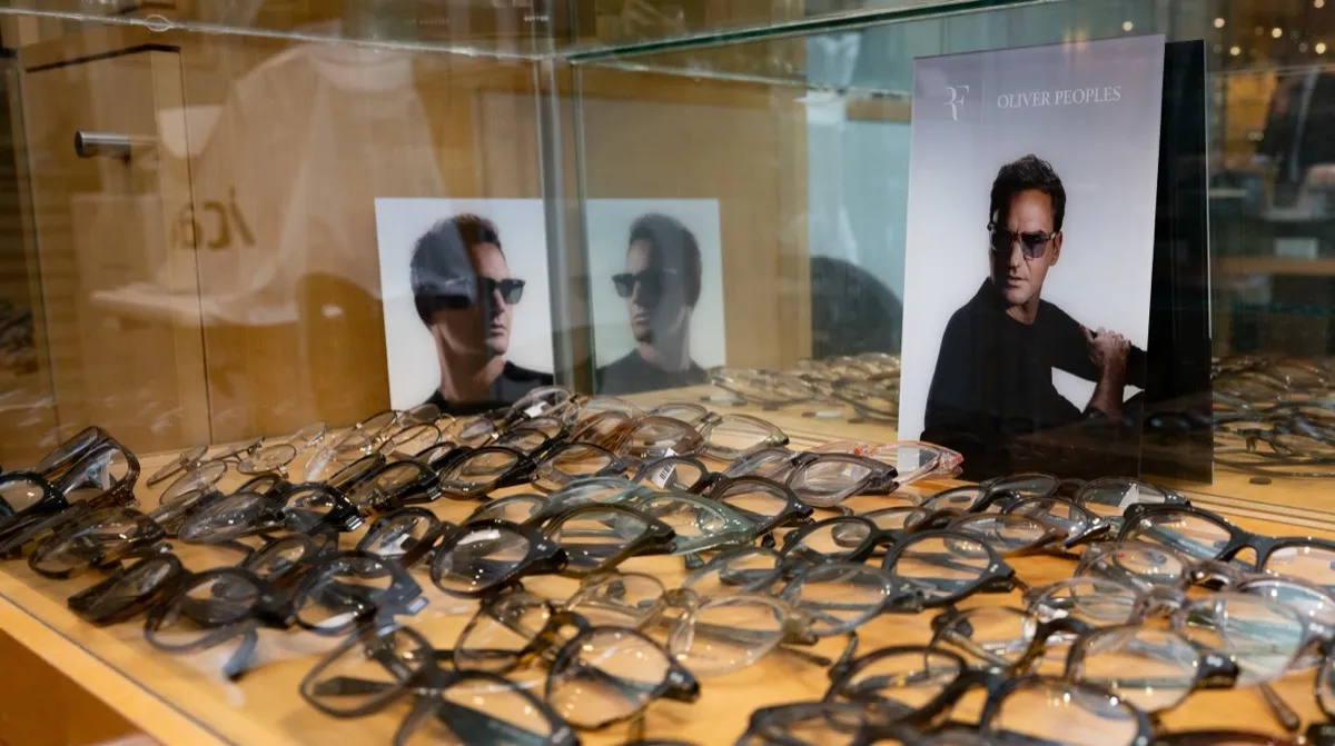 Oliver Peoples frames lined up in a lit display case beside a lookbook portrait at Voorthuis
