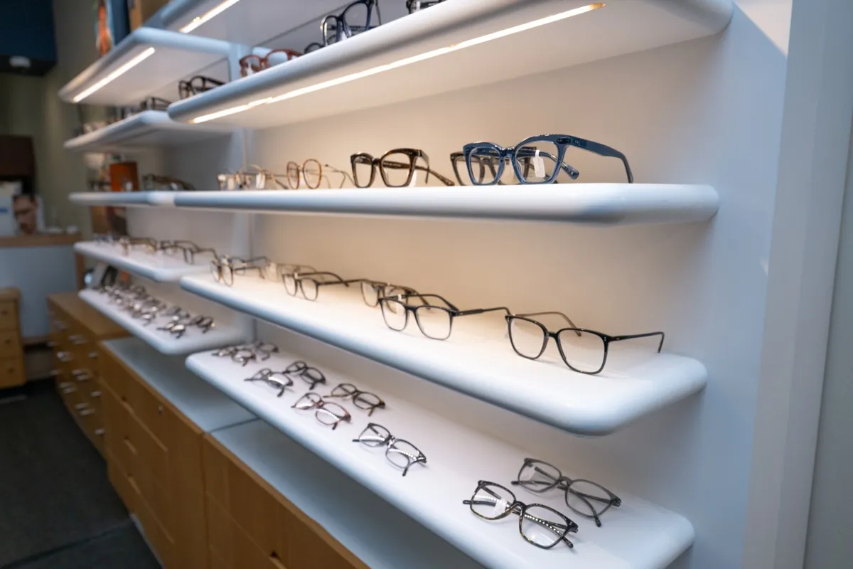 Oliver Peoples frames arranged on lit white display shelves at Voorthuis