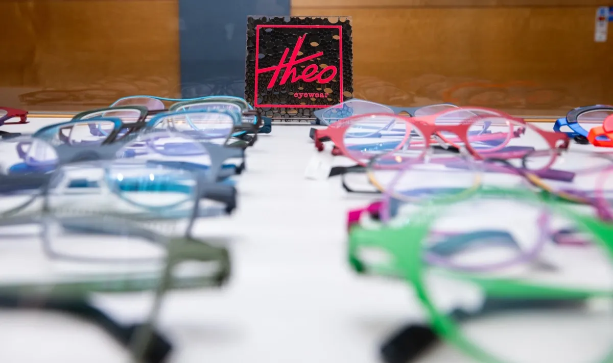 Rows of colorful Theo frames laid out beside the Theo eyewear display card at Voorthuis
