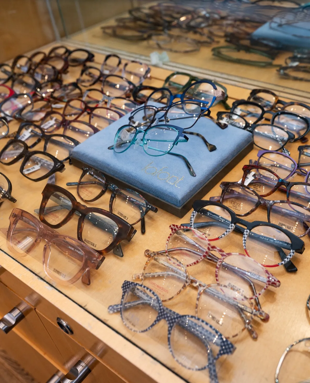 Designer eyeglass frames laid out on a wood display drawer at Voorthuis Opticians in Bethesda